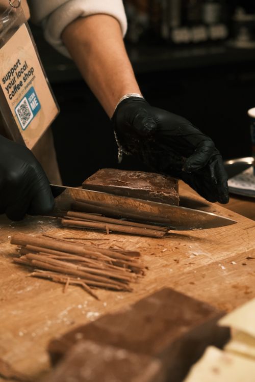 Free Close-up of a barista slicing chocolate in a café setting with a wooden board. Stock Photo