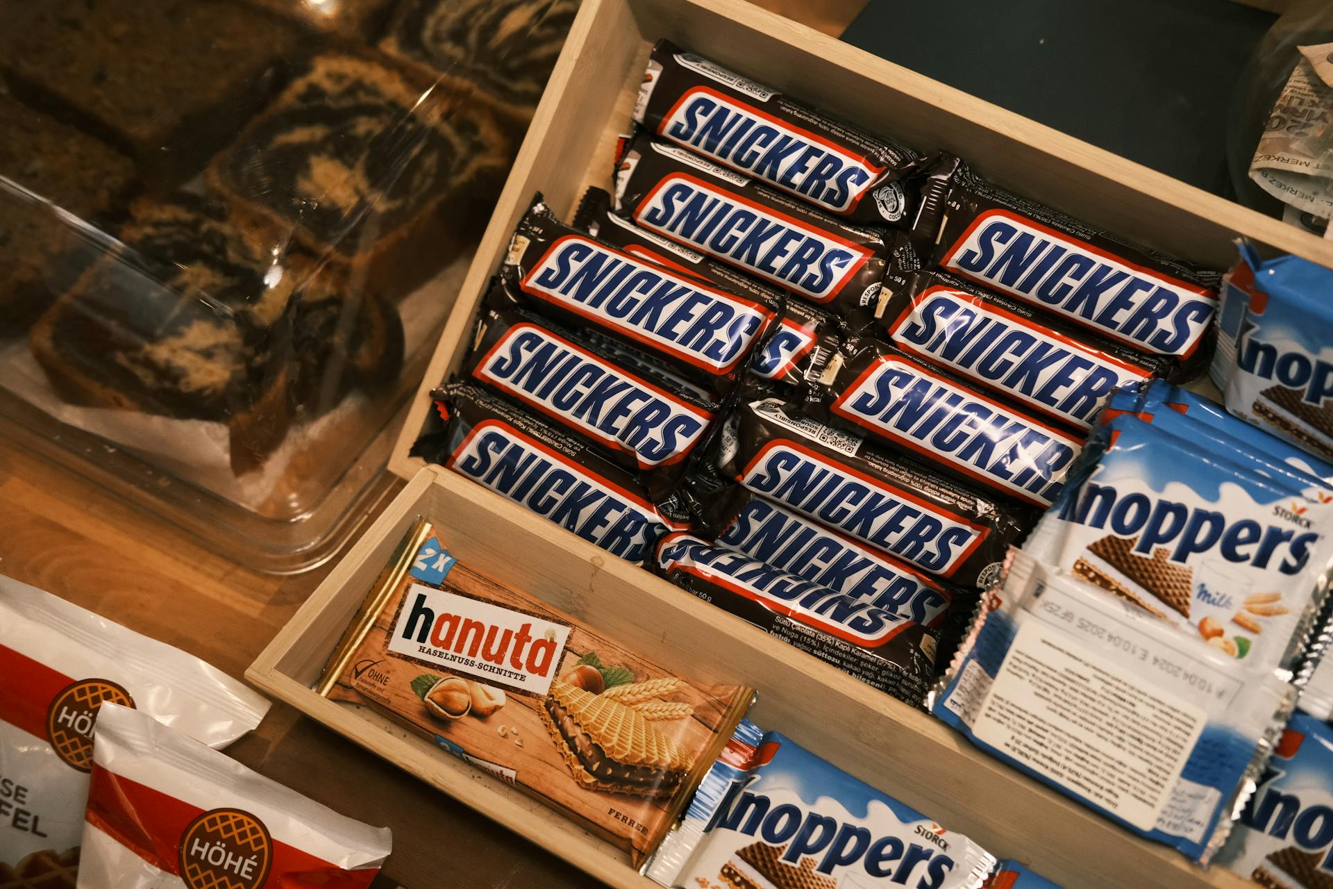 A variety of chocolate and wafer snacks including Snickers and Hanuta in a wooden box.