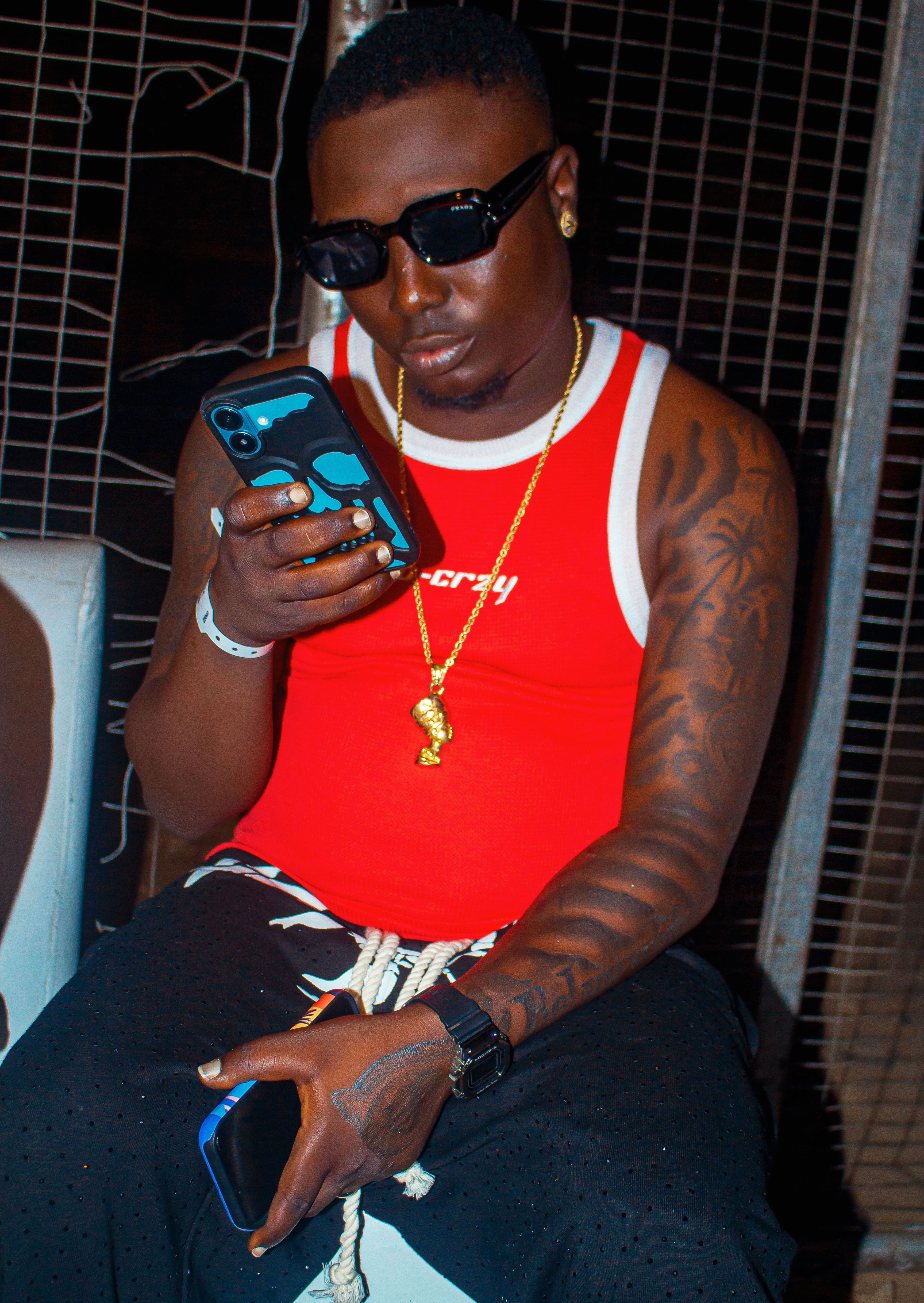 Trendy young man in a red tank top checking his phone at night.