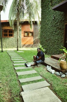 Man sitting on lush garden pathway in Ada Foah, Ghana. Serene and tropical setting.