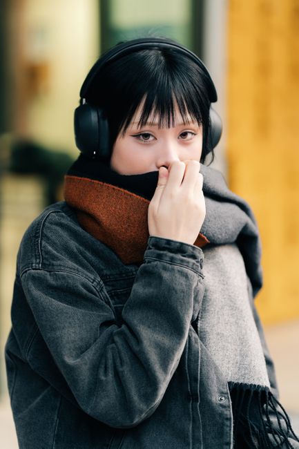 Portrait of a young woman wrapped in a scarf, wearing headphones, standing outdoors.