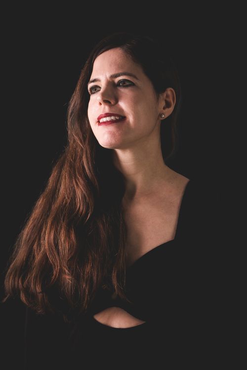 Free Elegant portrait of a young woman with long hair smiling against a dark background. Captivating and graceful. Stock Photo