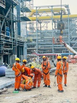 Group of construction workers in orange uniforms operating at an industrial site.