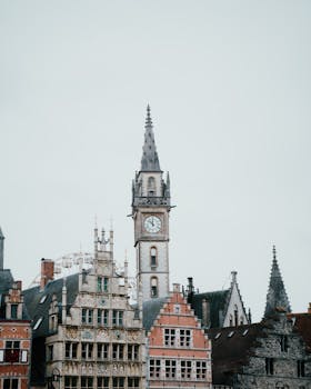 Majestic Ghent cityscape featuring a striking clock tower and historical buildings under a cloudy sky.