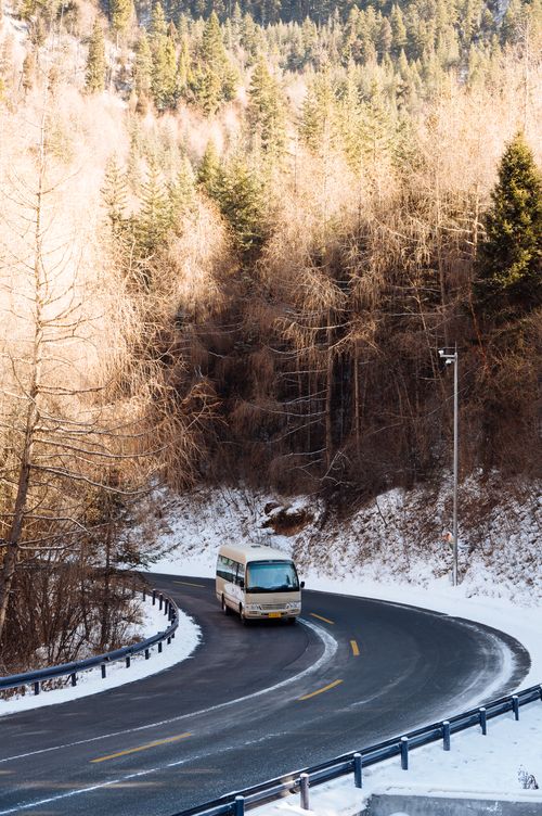 Free Minibus navigating a curved road through a snow-covered forest during winter, capturing serene natural beauty. Stock Photo