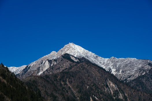 A stunning view of a snow-covered mountain peak with a vibrant blue sky in the background.