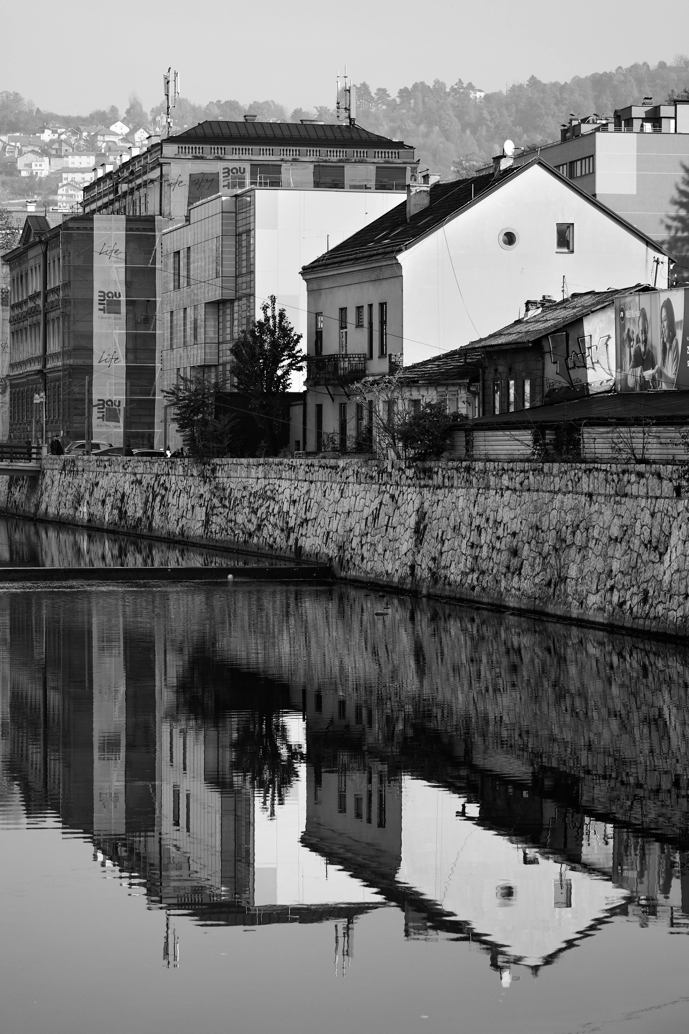 Black and white reflection of Sarajevo architecture on a calm river.