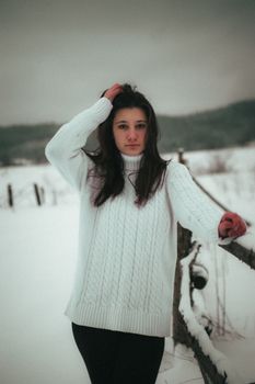 A young woman in a cozy sweater stands outdoors in a snowy Ukrainian landscape, exuding a warm, moody vibe.
