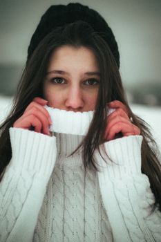 A moody winter portrait of a young woman in a cozy sweater, capturing a warm and intimate atmosphere.