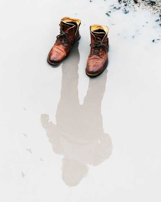 Brown leather boots with a reflection in a puddle, showcasing artistic composition.