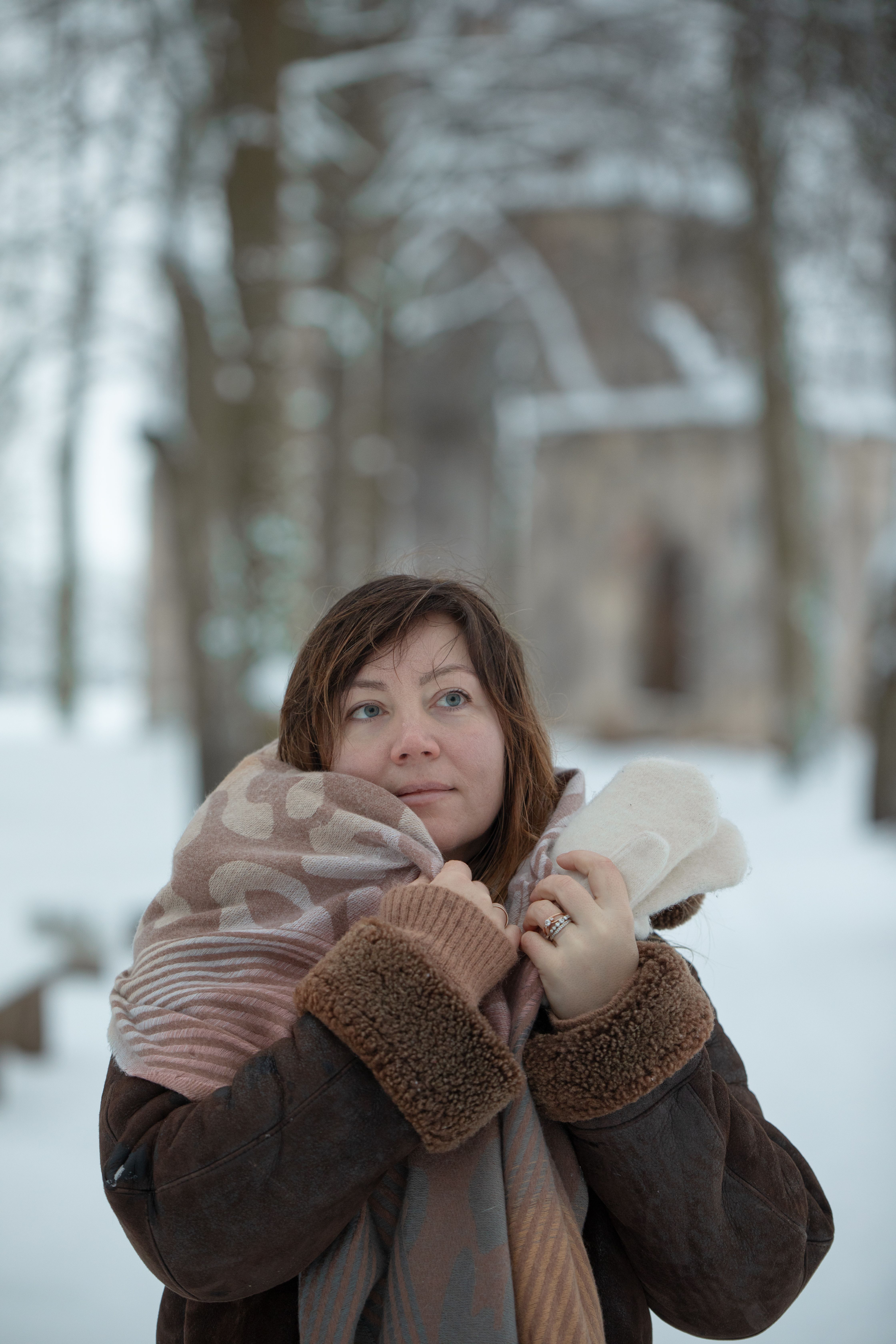 A woman enjoys the winter outdoors wrapped in a warm scarf against a snowy backdrop.