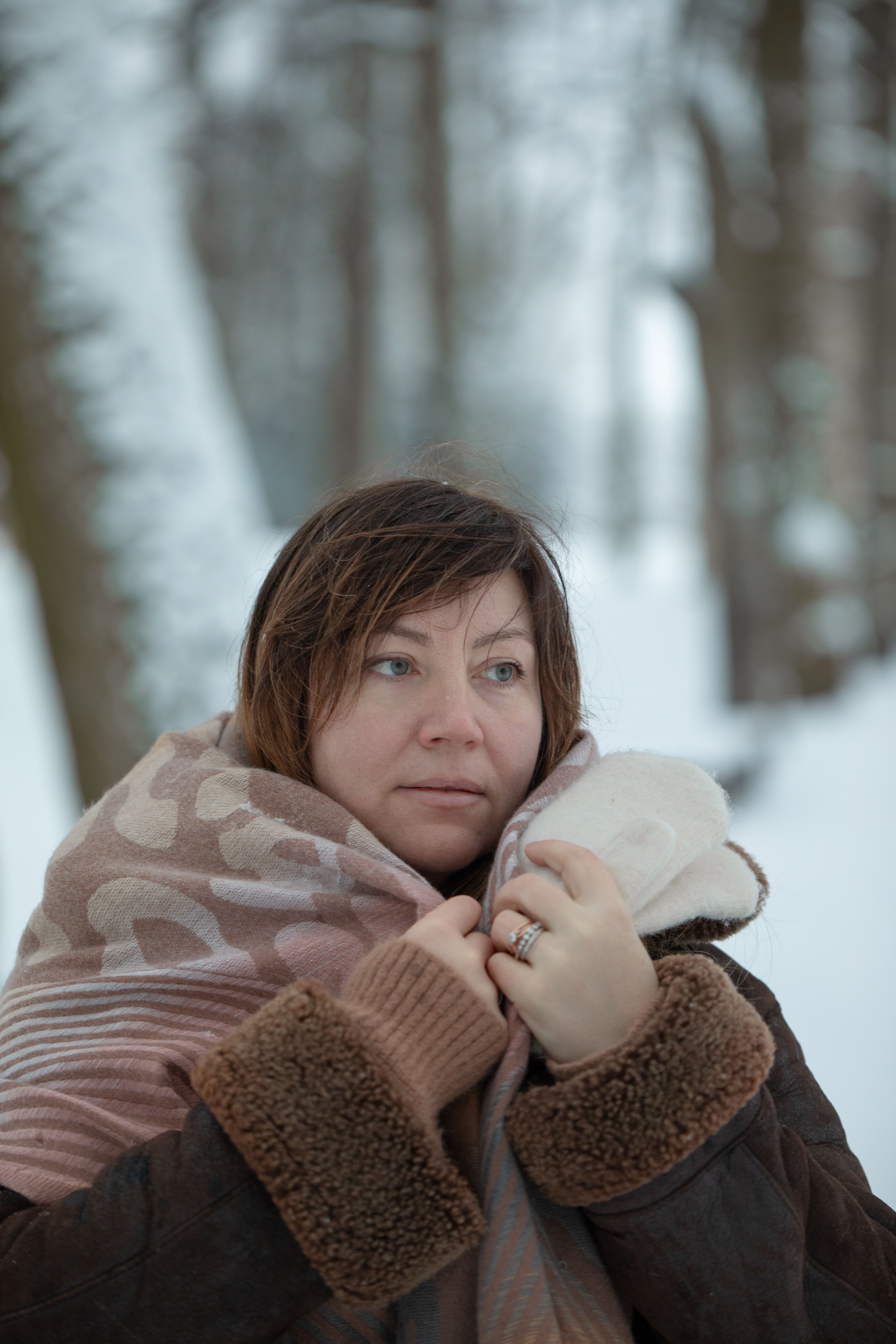 Adult woman wrapped in a cozy scarf enjoying the serene winter forest. Perfect for seasonal themes.