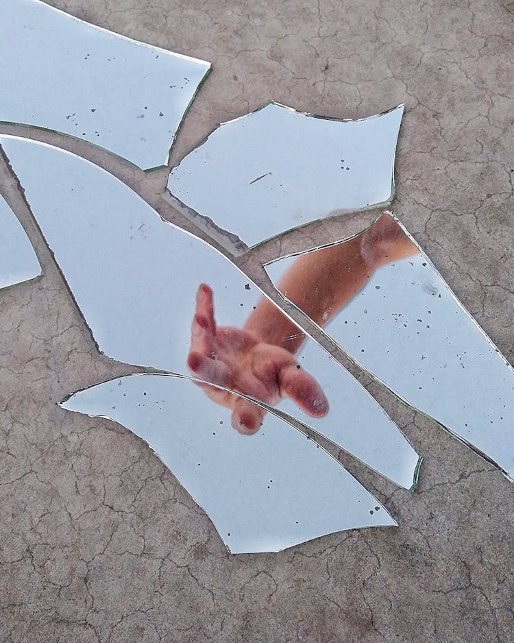 Mirror Fragments On Gray Surface With The Reflection Of A Person's Hand