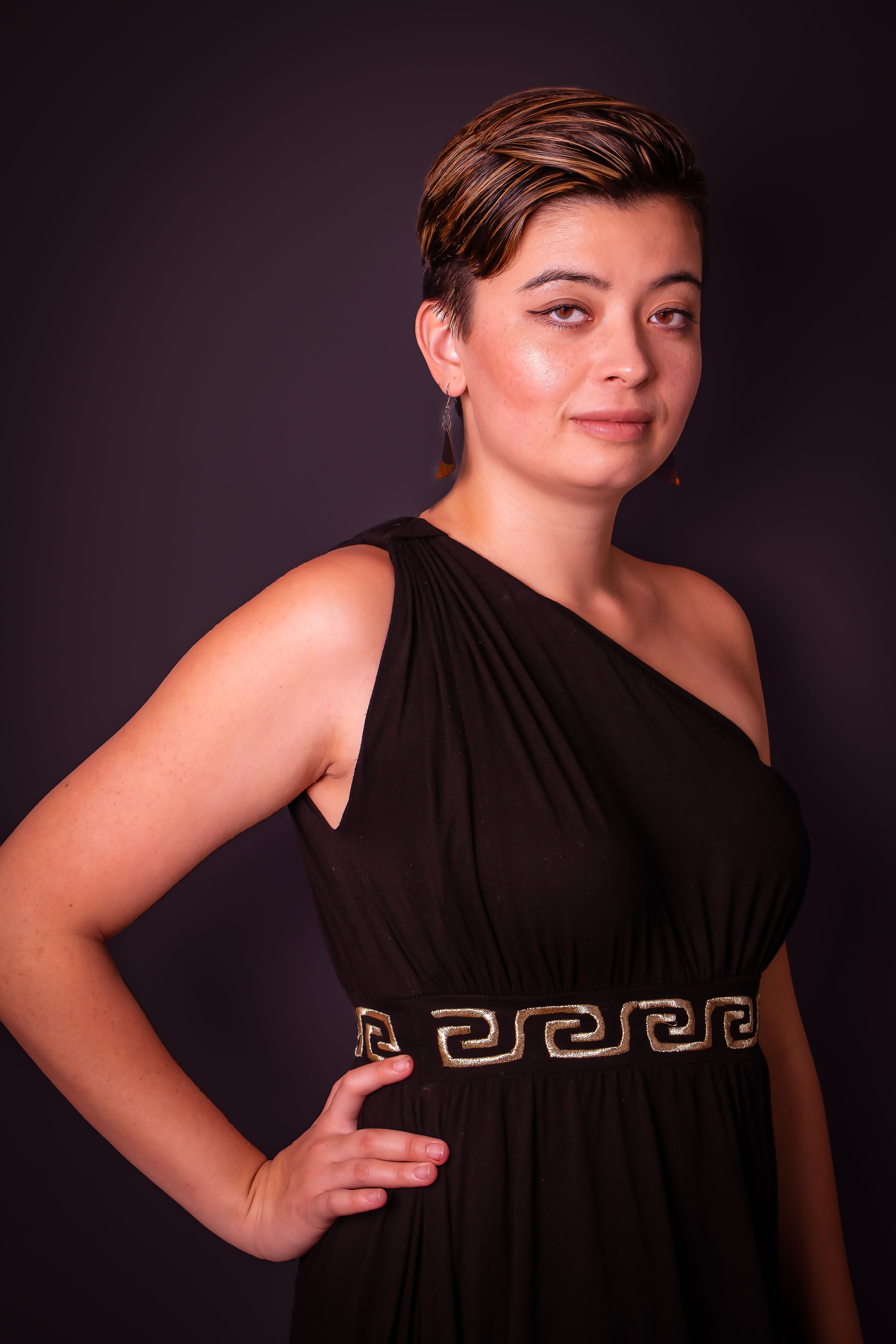 Portrait of a confident woman in a black dress with Greek key design, dark background.