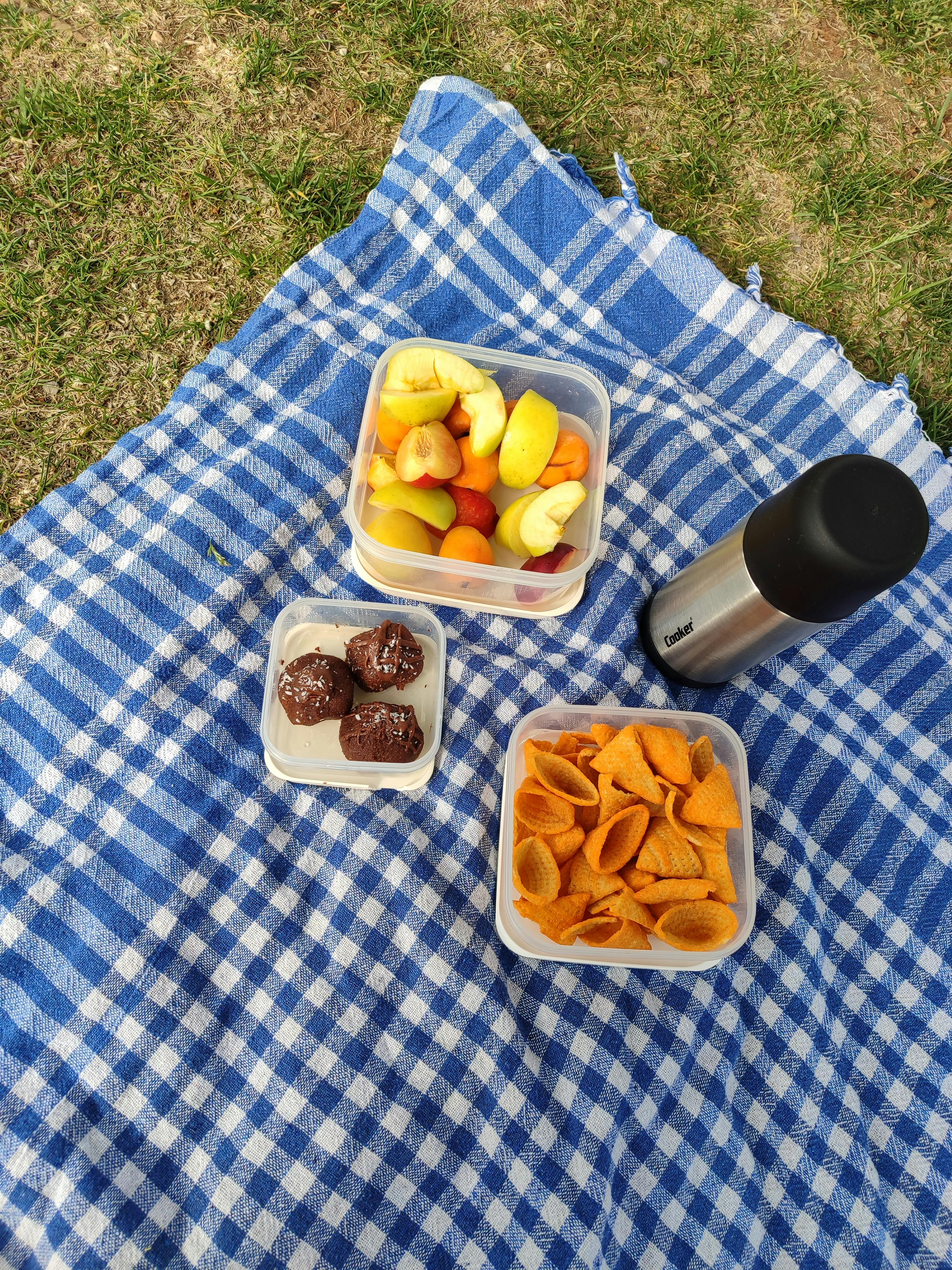 Tasty assortment of snacks and fruits on a blue picnic blanket outdoors.