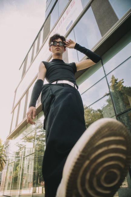 Stylish young man in urban outfit poses confidently outdoors by modern building.