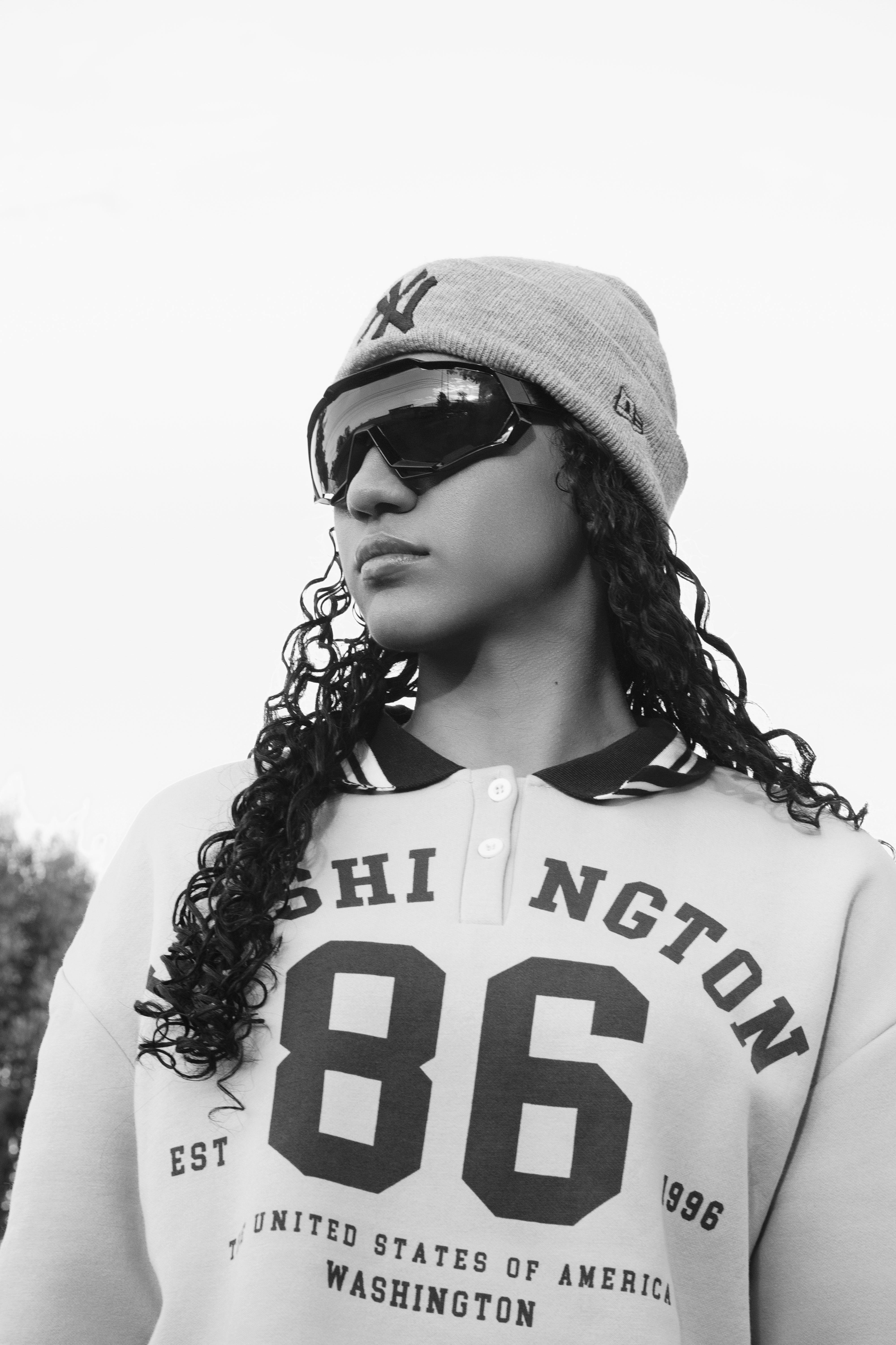 Stylish black and white portrait of a young adult in sunglasses and a casual outfit outdoors.