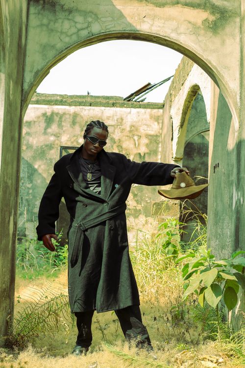 Free Man in a dark coat posing with a hat in an old, overgrown building. Stock Photo