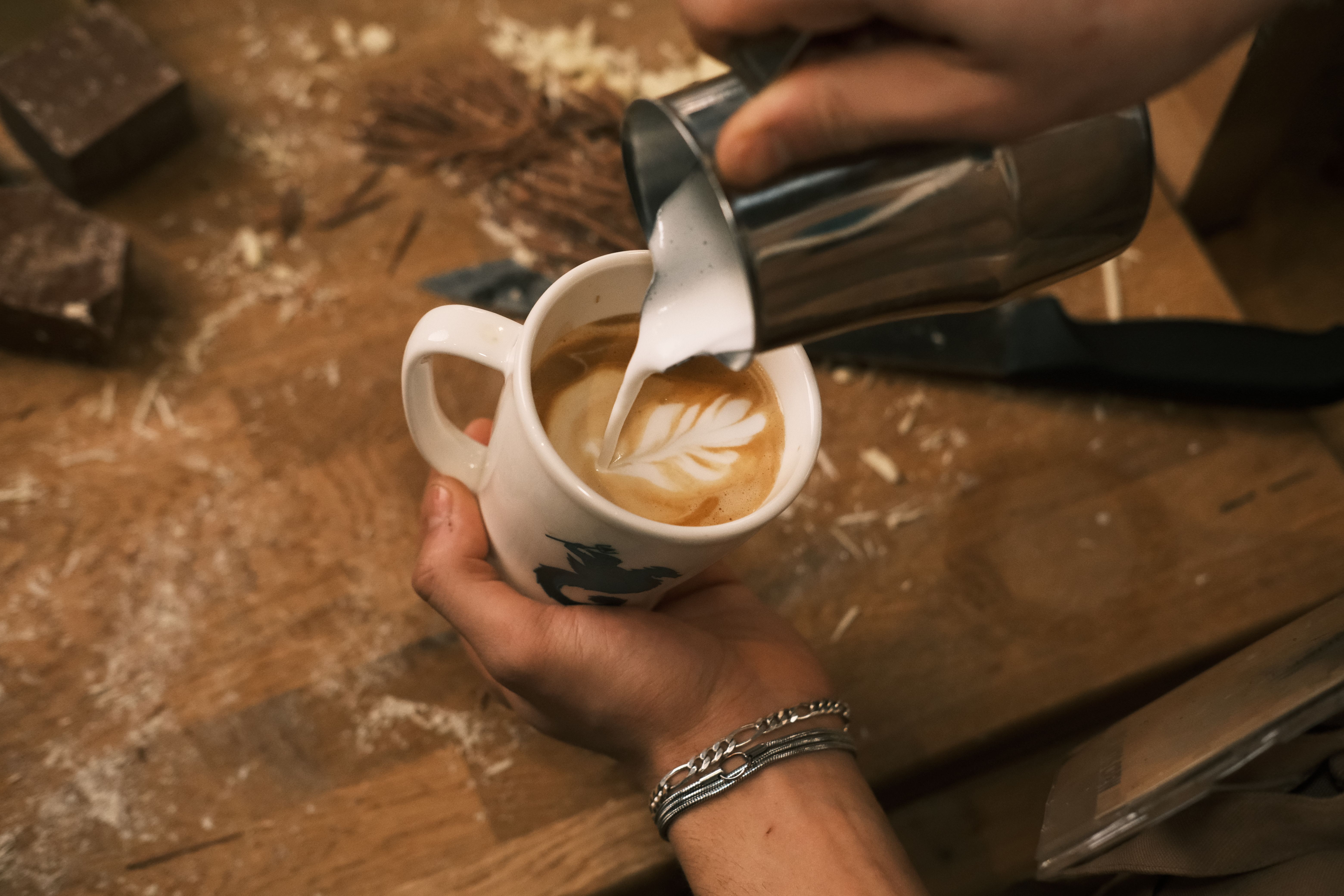 Gros plan des mains d'un barista versant du lait dans une tasse de café dans un café confortable de Konya.