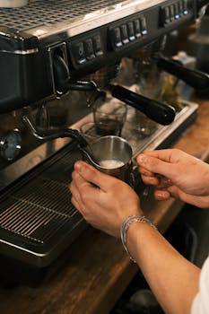 Barista preparing milk foam at an espresso machine in a cozy café setting.