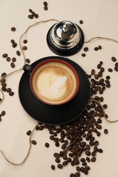 A top-down view of a frothy coffee cup surrounded by beans and a service bell.