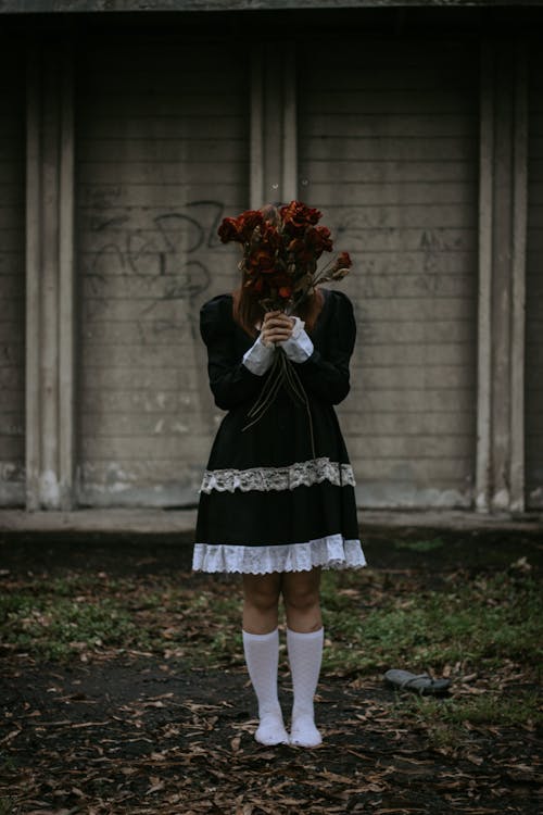 Woman in Dress and White Tights Hiding Face Behind Bouquet of Red Flowers
