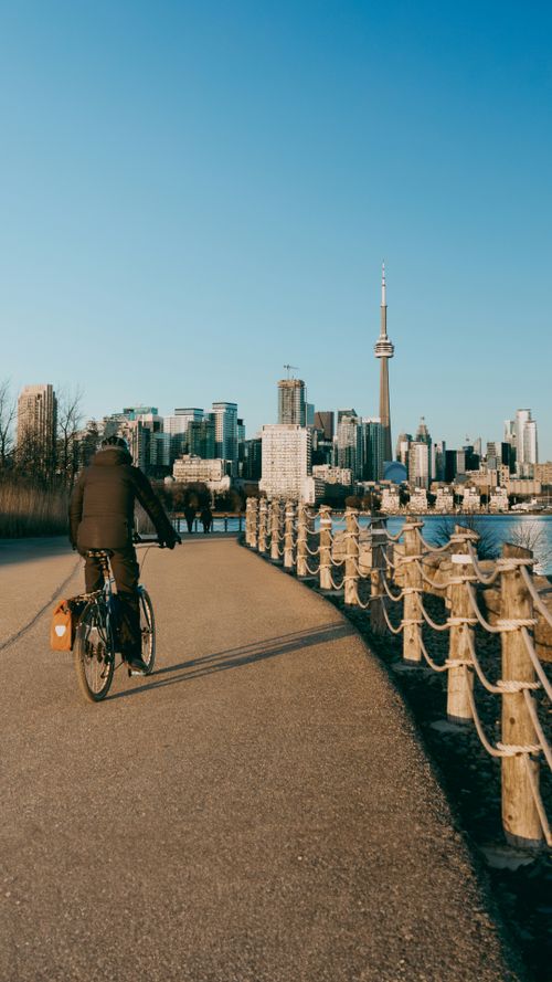 Free Cyclist on a path by water with Toronto skyline and CN Tower in view during daytime. Stock Photo