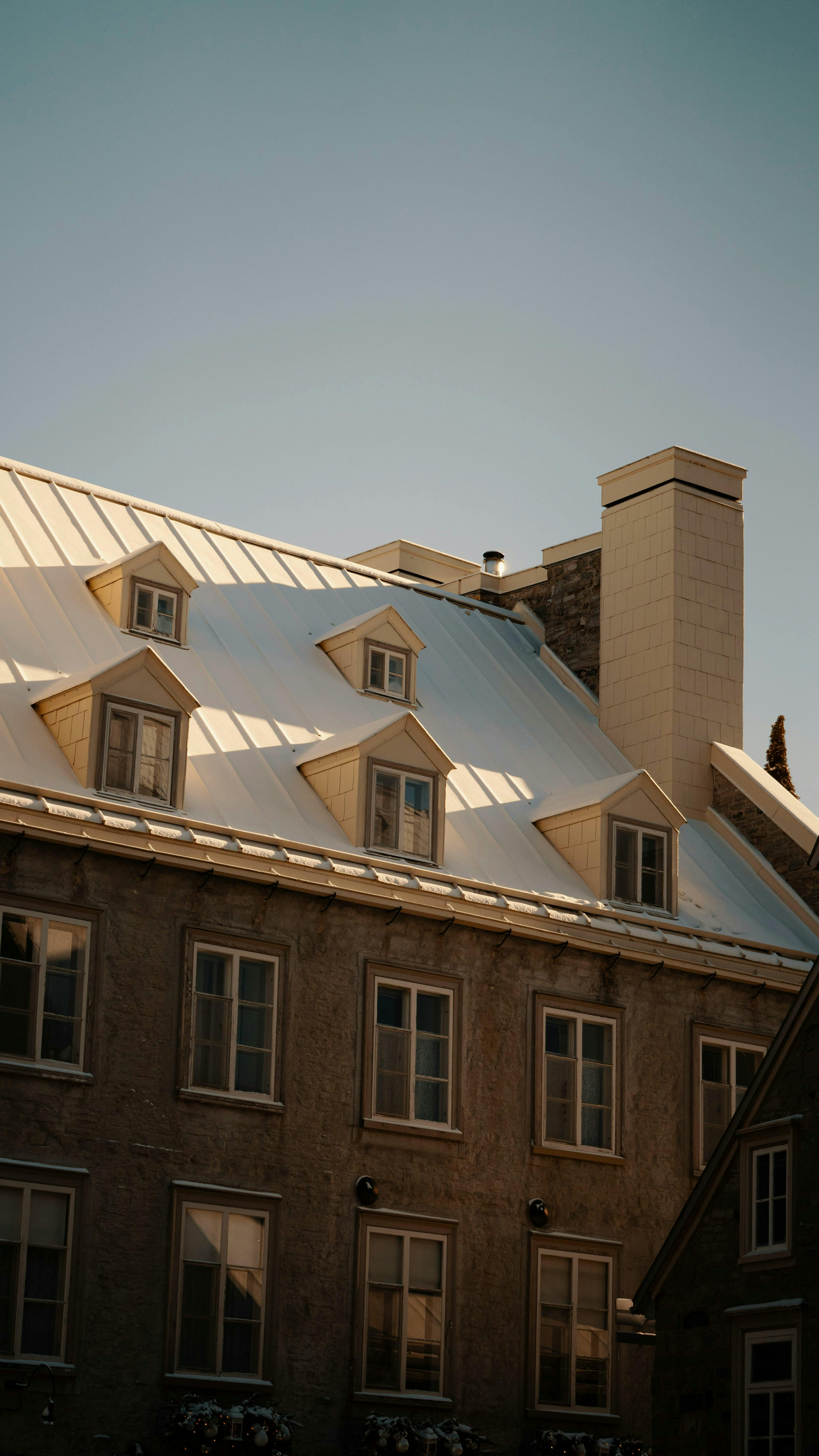 A vintage building with a sloped metal roof under a clear sky, capturing warm sunlight and shadow play.