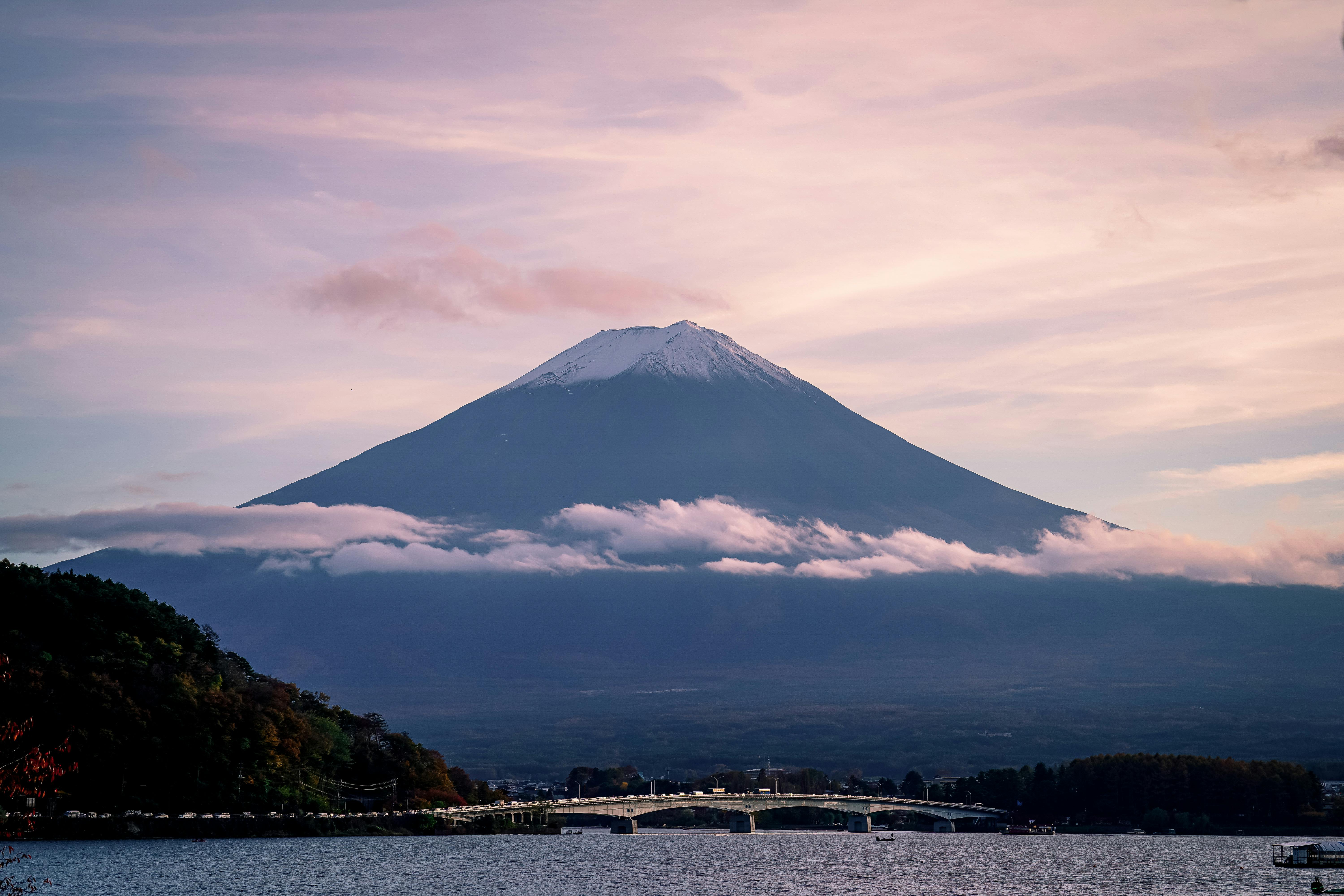 A breathtaking view of Mount Fuji with delicate clouds and serene waters beneath a pastel sky.