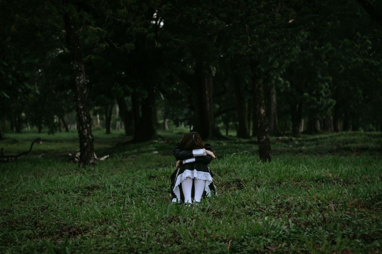 a woman in a black dress sits on grass in a moody surreal forest setti