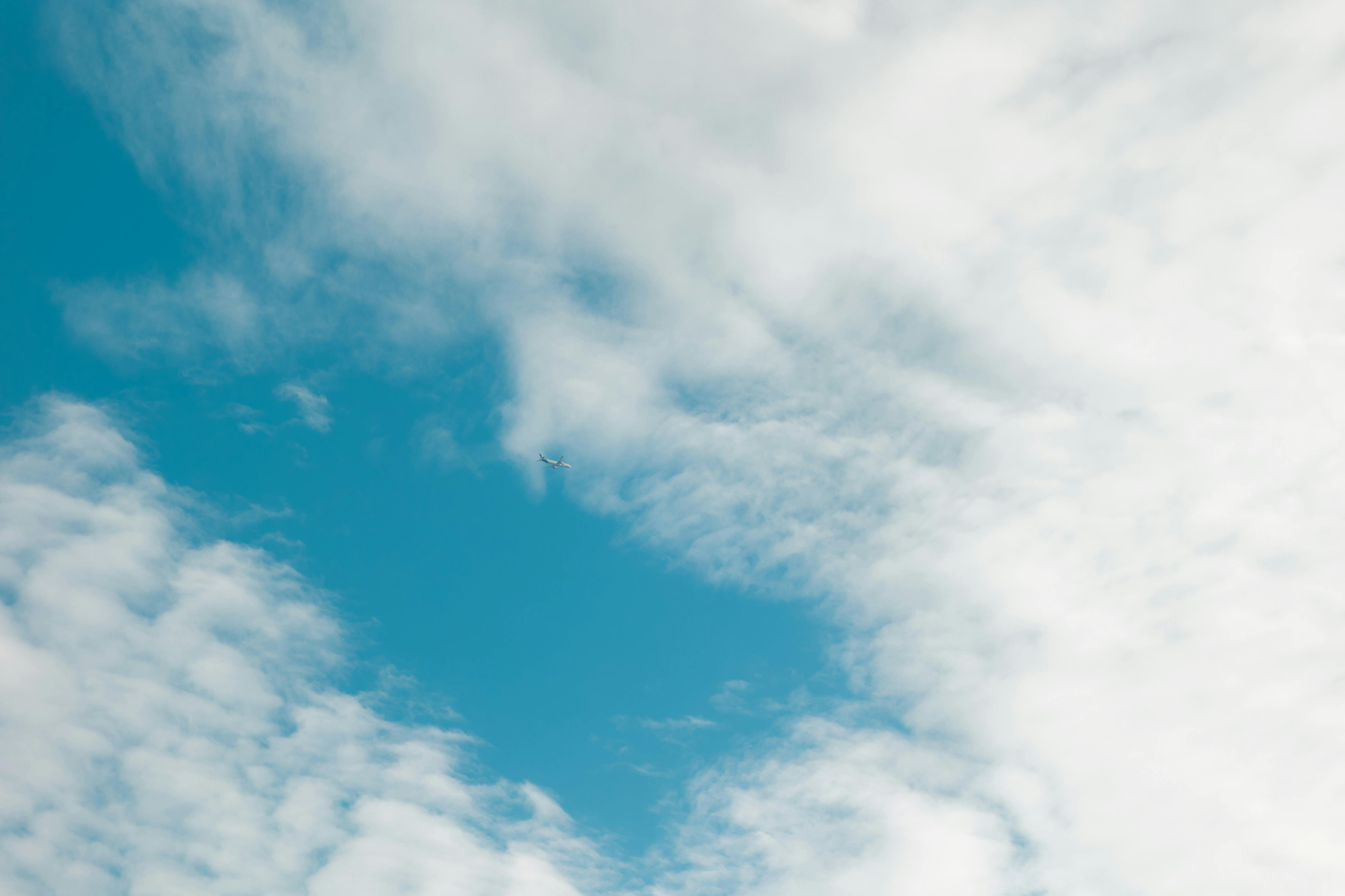 Gratis Una escena tranquila de un cielo azul con nubes tenues y un pequeño avión en la distancia, que evoca una sensación de calma y pasión por los viajes. Foto de stock