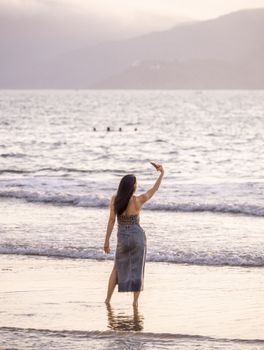 A woman enjoys the sunset while taking a selfie on the beach in Quy Nhơn, Vietnam.