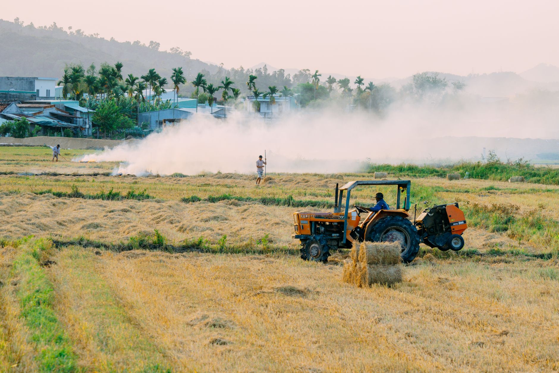 A typical rural scene in Quy Nhơn, Vietnam, showing a tractor in a field with smoke in the background.