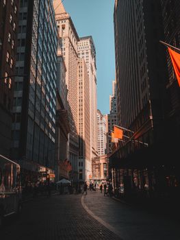 Sunlit street in New York City with towering skyscrapers and bustling pedestrian life.