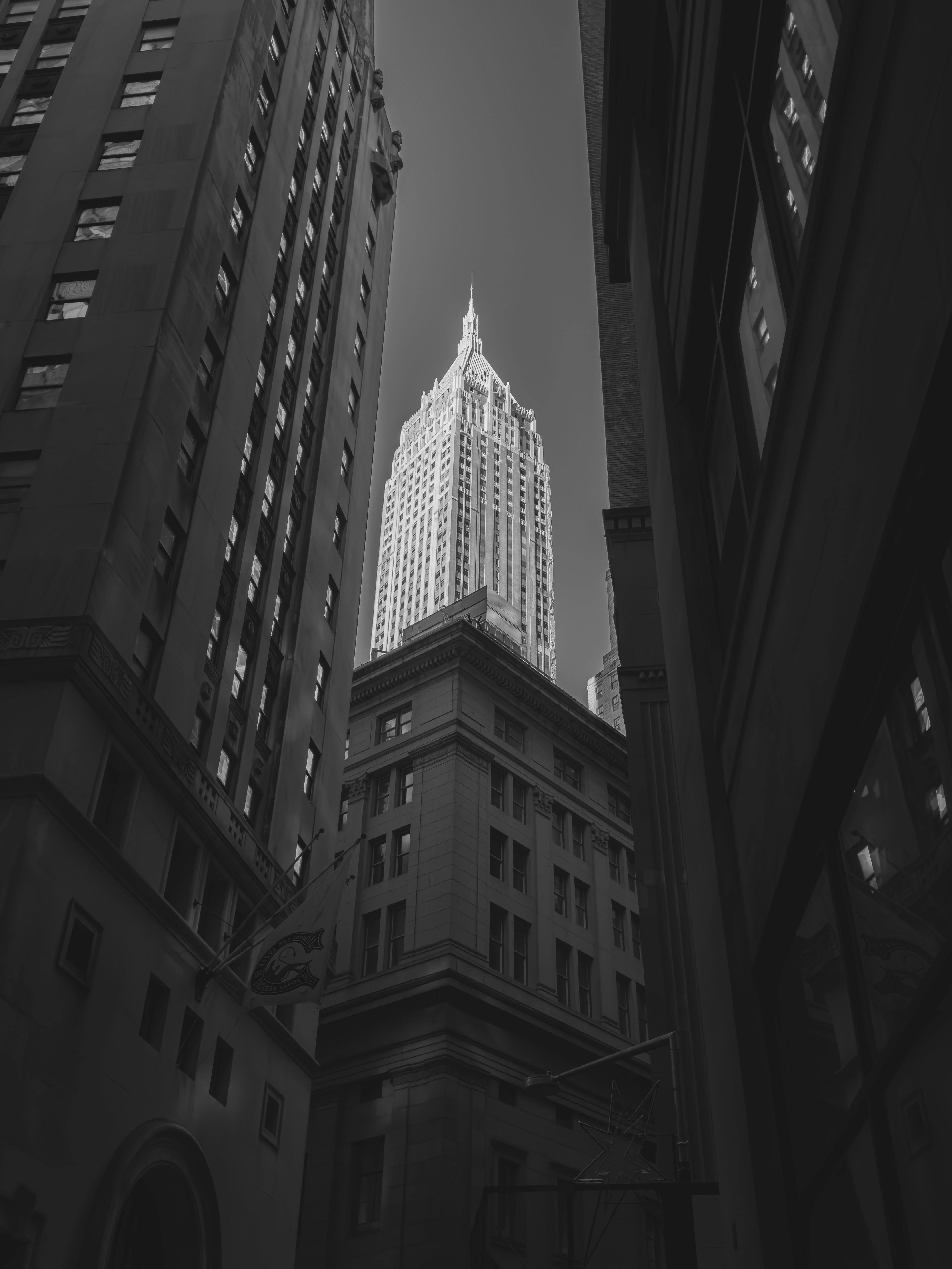 Black and white view of the Empire State Building nestled among towering Manhattan skyscrapers.