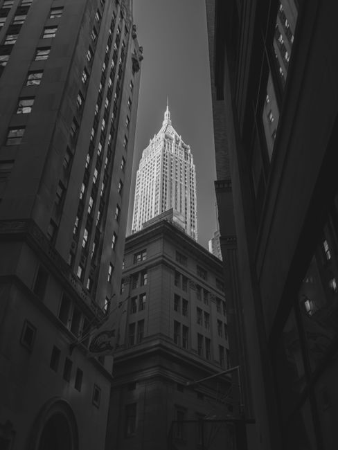 Black and white view of the Empire State Building nestled among towering Manhattan skyscrapers.