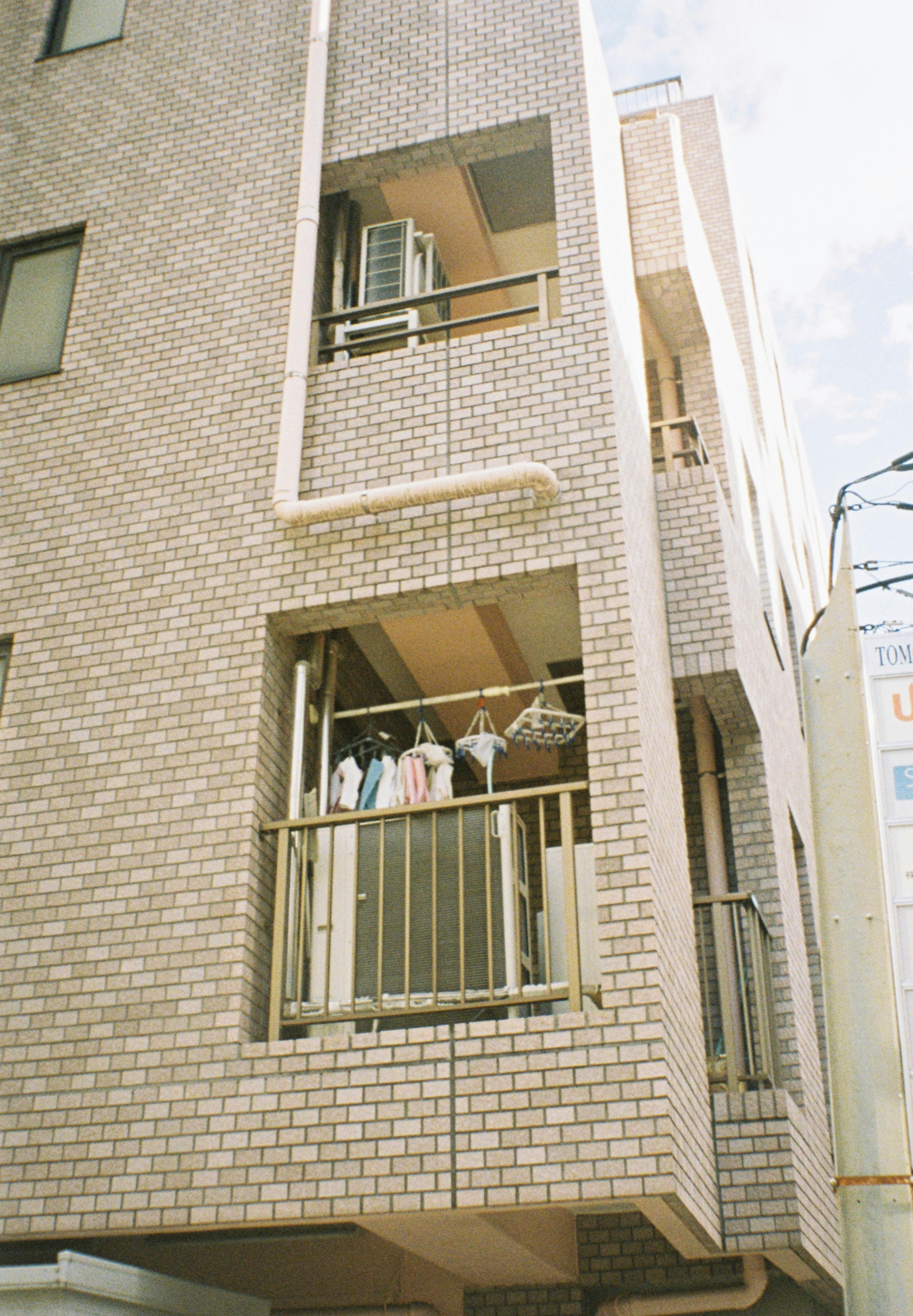 Gratis Apartemen kota dengan pakaian yang dijemur di balkon dengan latar belakang perkotaan yang cerah. Foto Stok