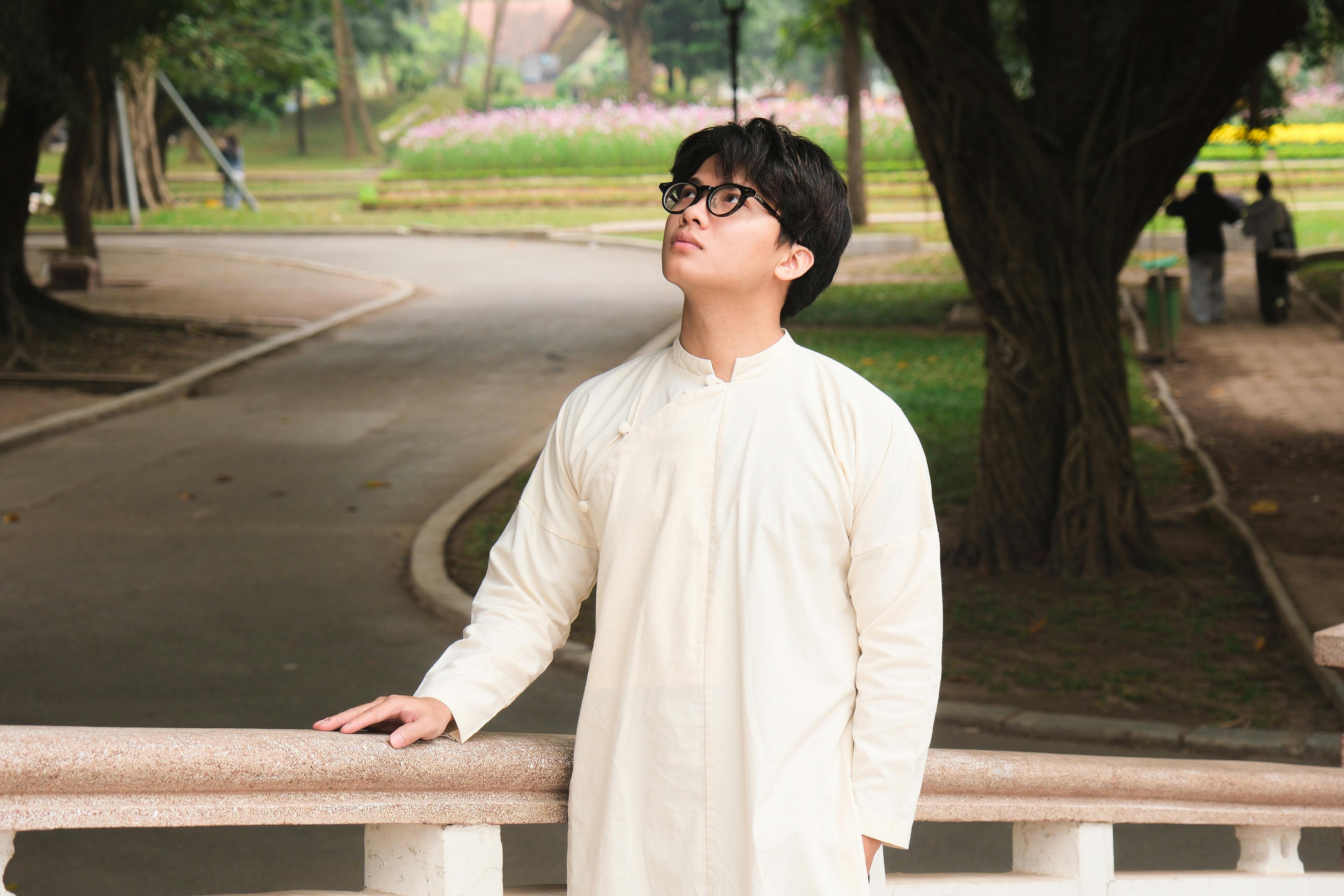 Young man in traditional clothing, looking thoughtful in a park setting.