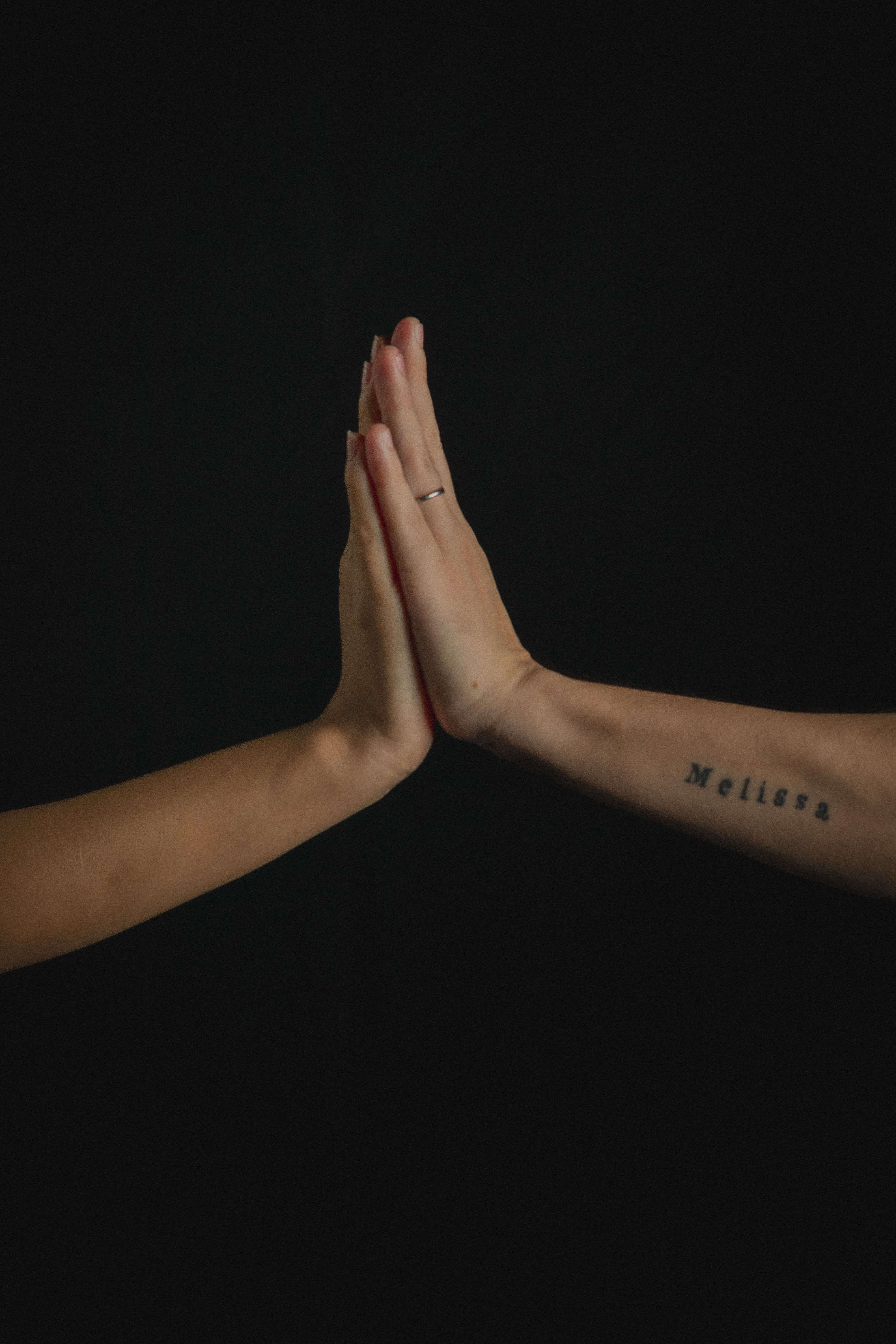 Two hands touching with tattoos and rings, symbolizing connection and intimacy.