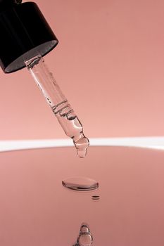 A dropper releasing liquid onto a reflective surface with a pink backdrop.