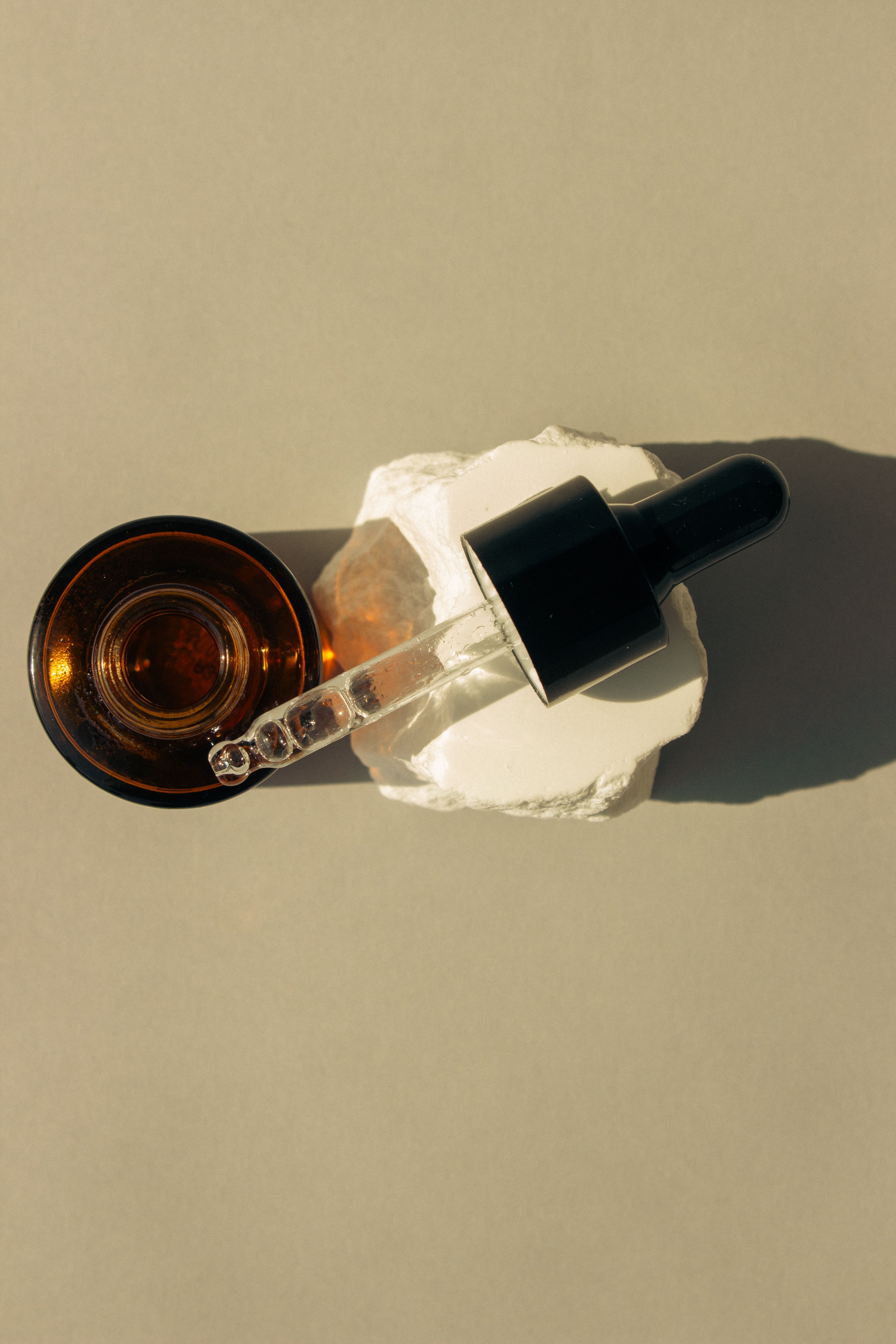 Radiance Renewal Serum dropper bottle on white stone in warm sunlight