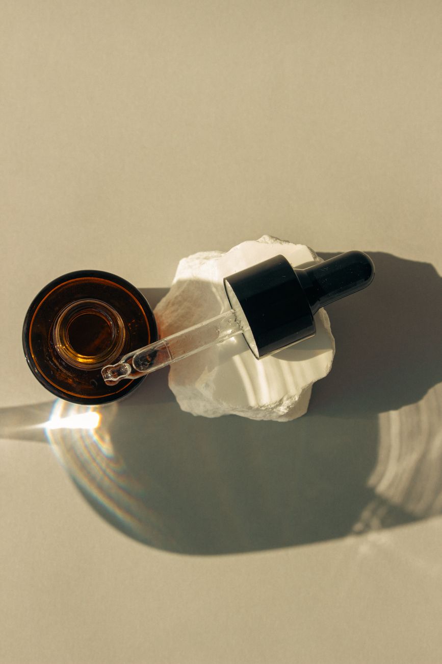Stylish dropper bottle with skincare liquid on a ceramic surface, casting artistic shadows.