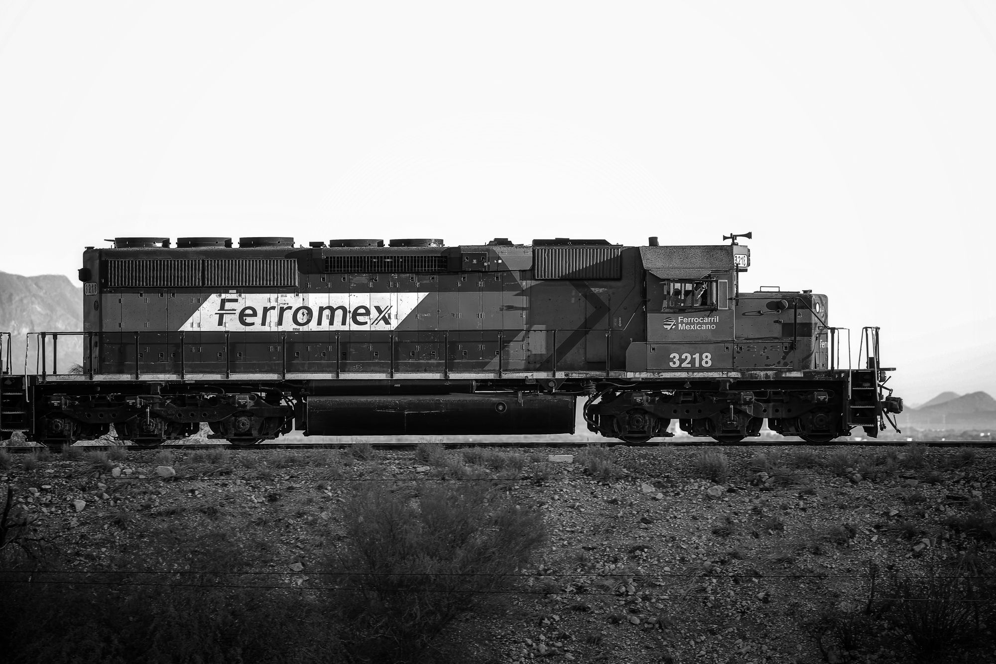 A black and white image of a Ferromex train in a desert landscape.