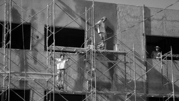 Construction workers on scaffolding in black and white, showing teamwork and safety.