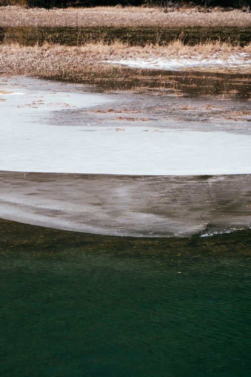 Free A scenic view of a partially frozen river with distinct layers of ice and open water, captured in winter. Stock Photo
