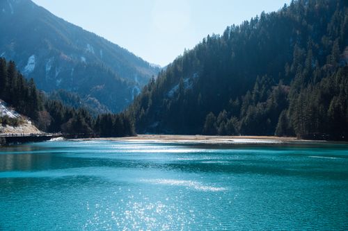 Free Crystal clear lake surrounded by lush green forested mountains under a bright sky. Perfect serene landscape. Stock Photo