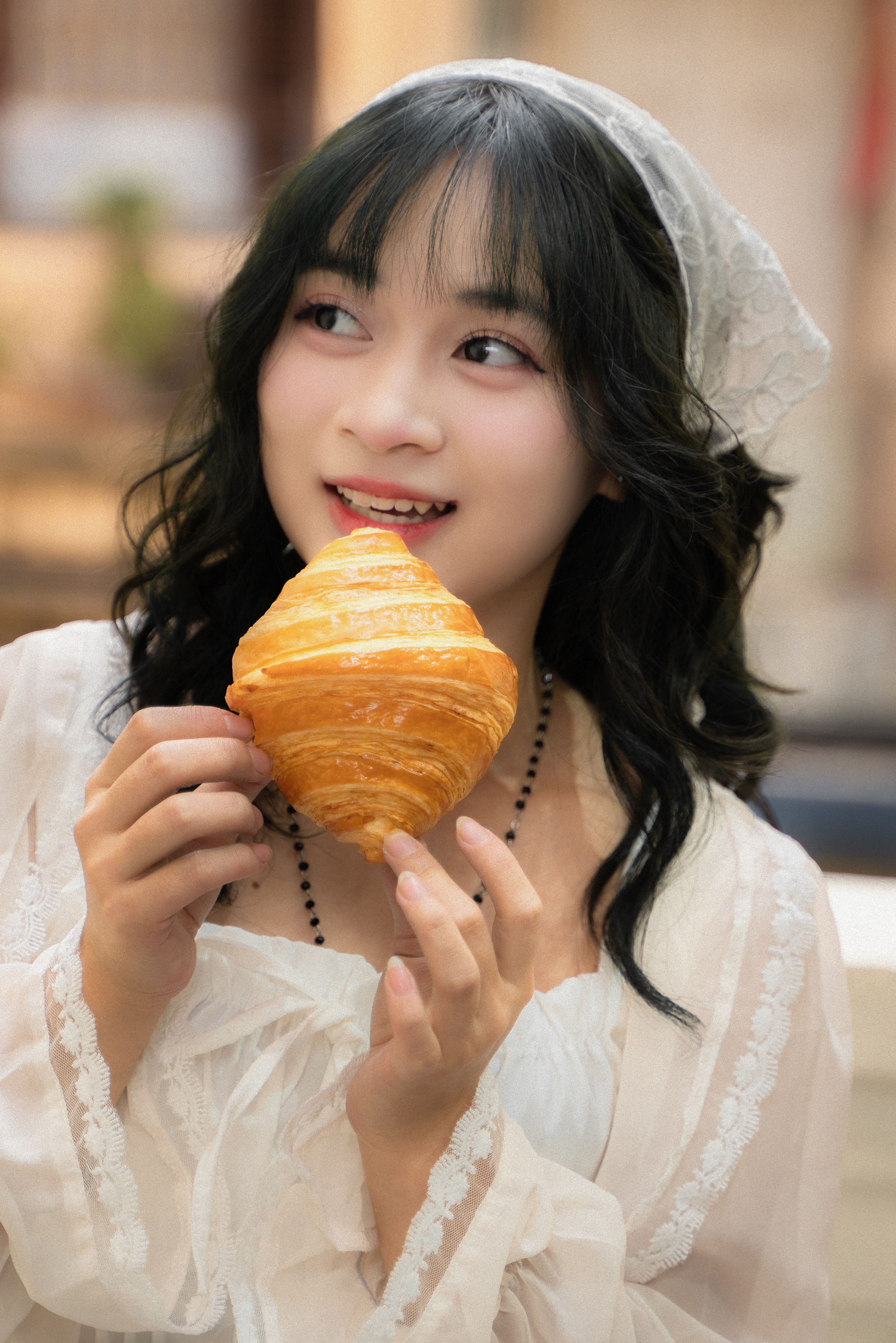 Young woman smiling while holding a croissant in a cozy cafe setting.