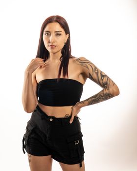 Portrait of a confident woman posing in studio, showcasing tattoos and modern fashion.