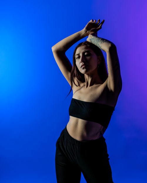 Free Portrait of a woman with tattoos posing against a colorful blue and purple studio background. Stock Photo