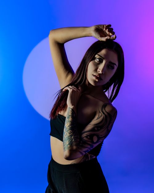 Free Portrait of a stylish woman with tattoos, posing confidently in a studio with a colorful background. Stock Photo